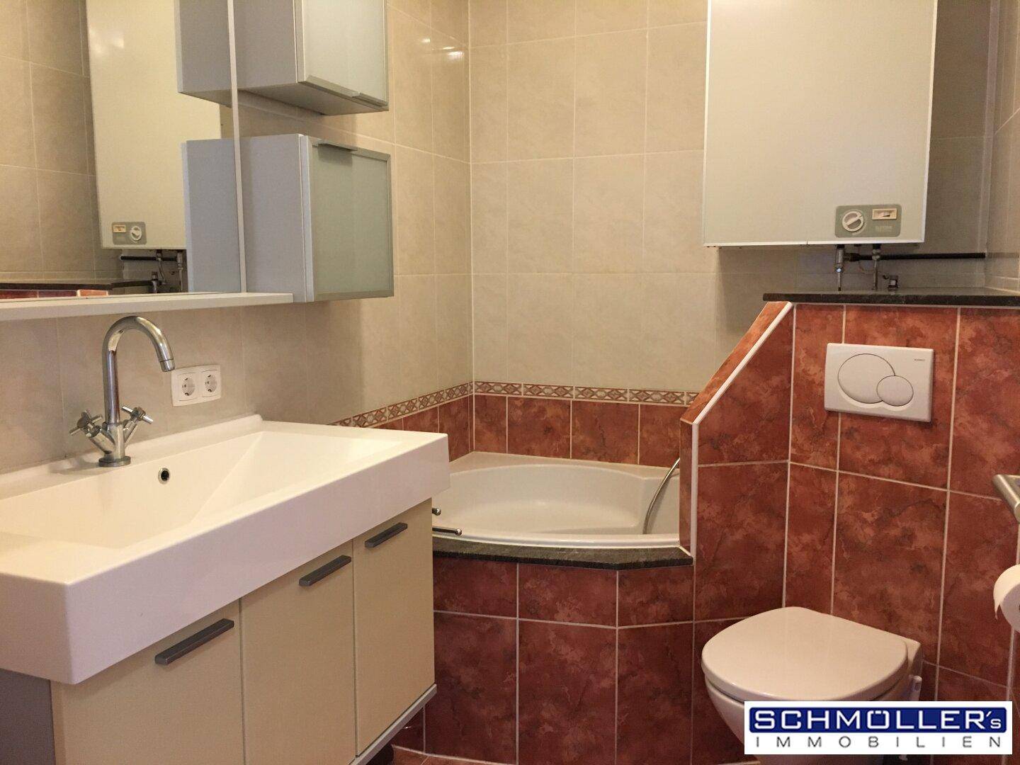Badezimmer mit Eckbadewanne, Einzelwaschbecken und Wand-WC, gefliest in warmen Farbtönen.