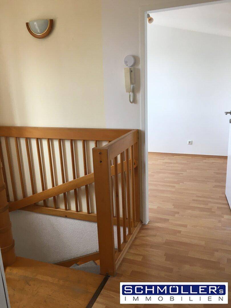 Holztreppe mit Geländer und Gegensprechanlage in einem hellen Wohnbereich.