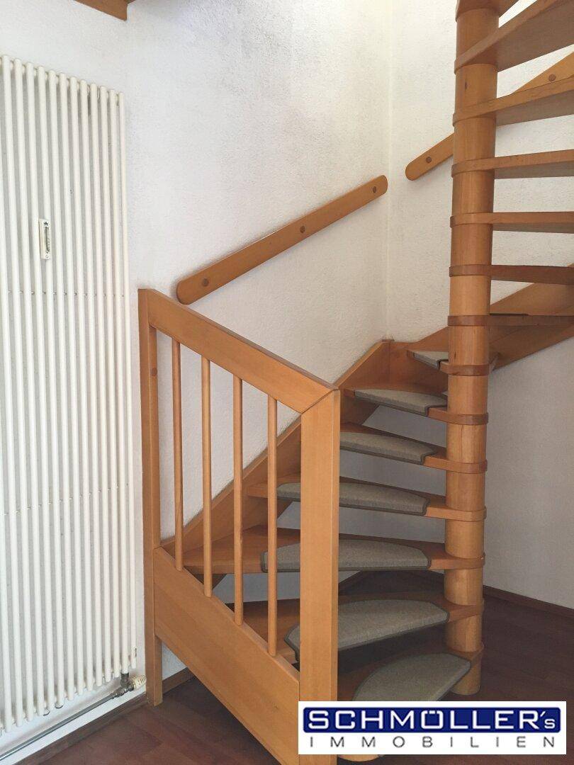 Helle Holzwendeltreppe mit Teppichstufen und Heizkörper in einem Wohnbereich.
