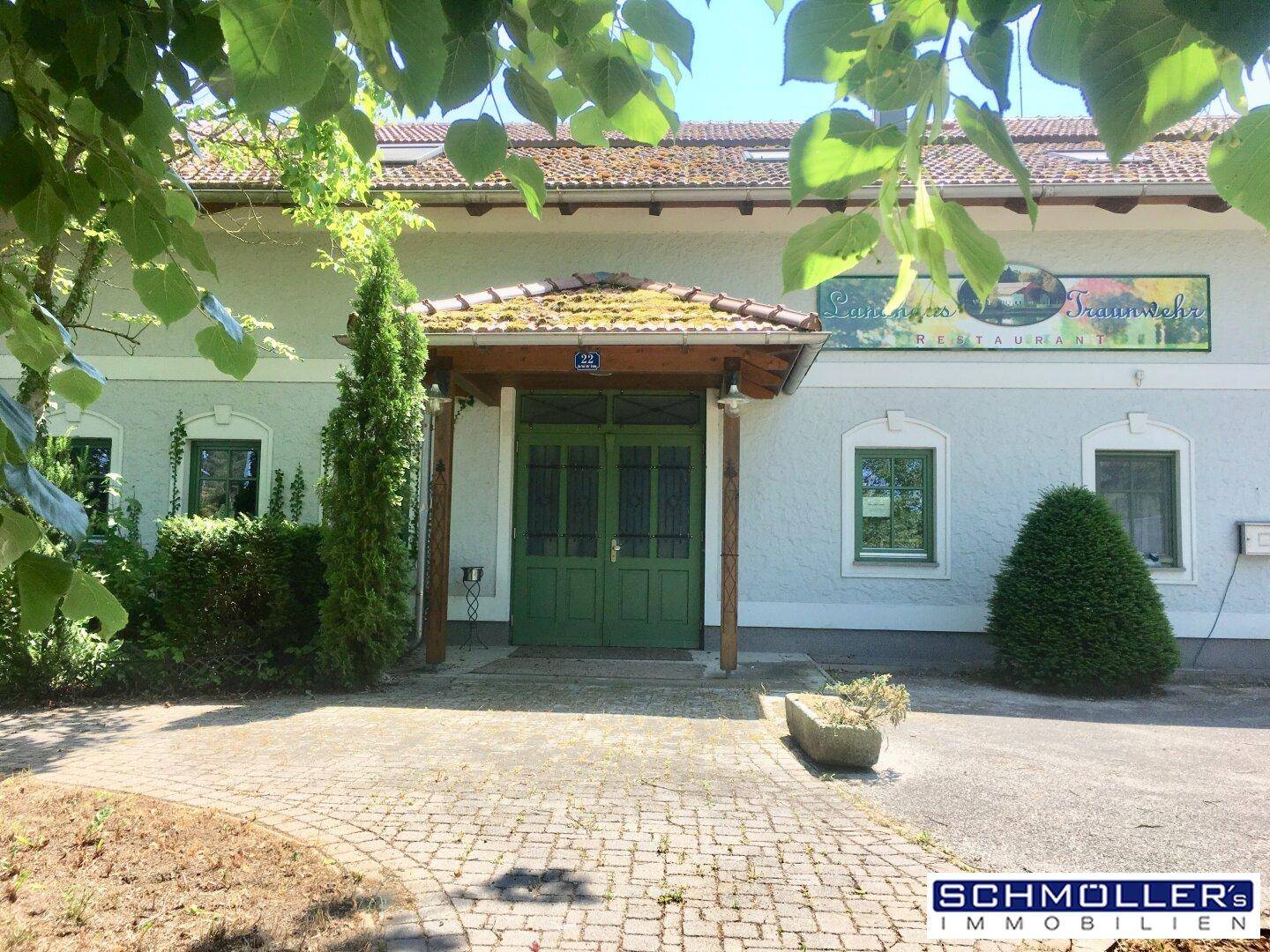 Hauptfassade des Landhauses mit dem grünen Eingangstor und einem gepflasterten Vorplatz.