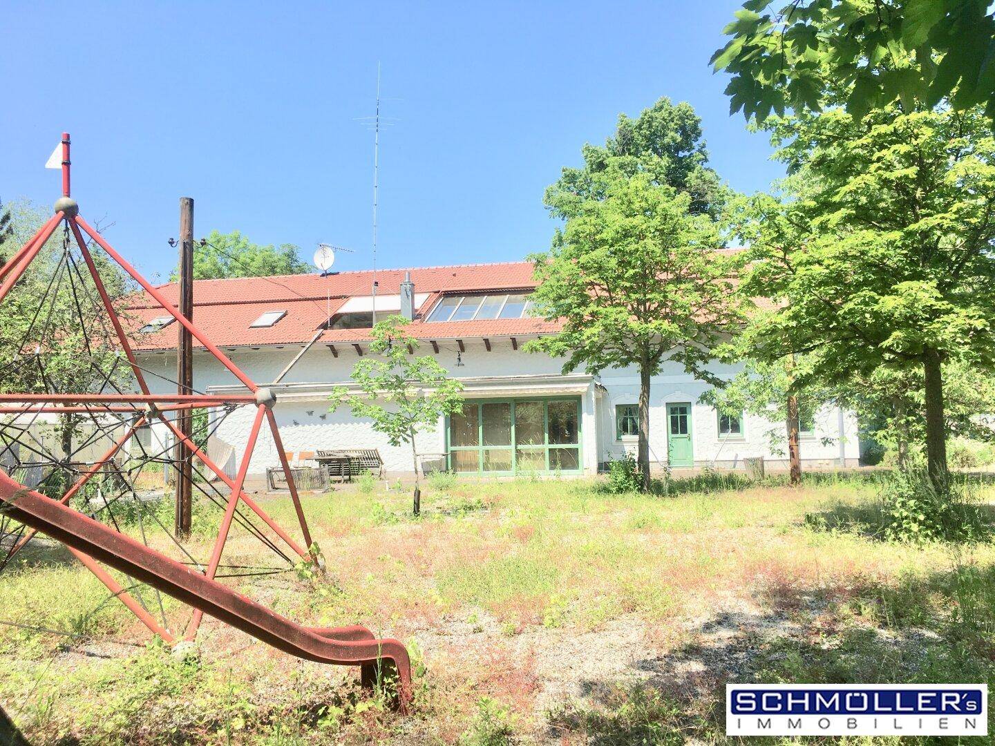 Hinteransicht des Gebäudes mit einem Spielplatz im Vordergrund und einer großen Rasenfläche.
