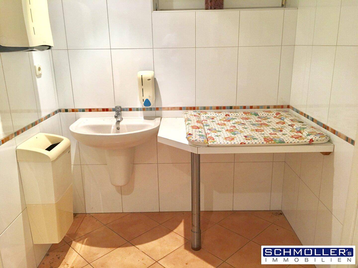 Badezimmer mit Wickeltisch, Waschbecken und weißen Fliesen, praktisch für Familien.