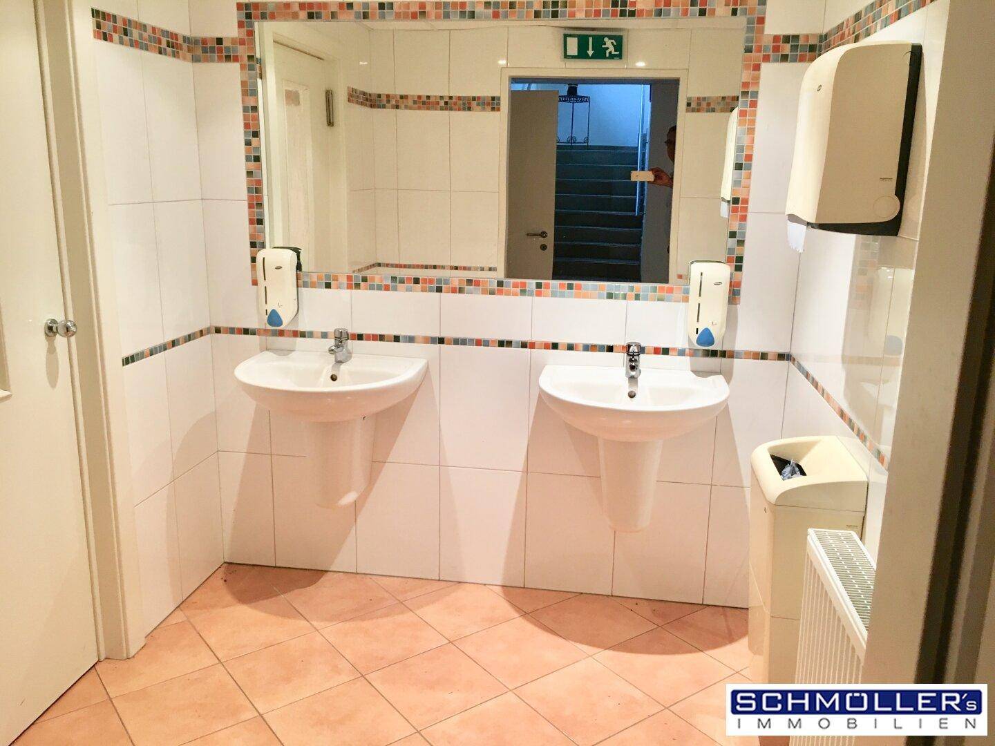 Geräumiger Waschraum mit zwei Waschbecken, großem Spiegel und Terrakotta-Fliesenboden.