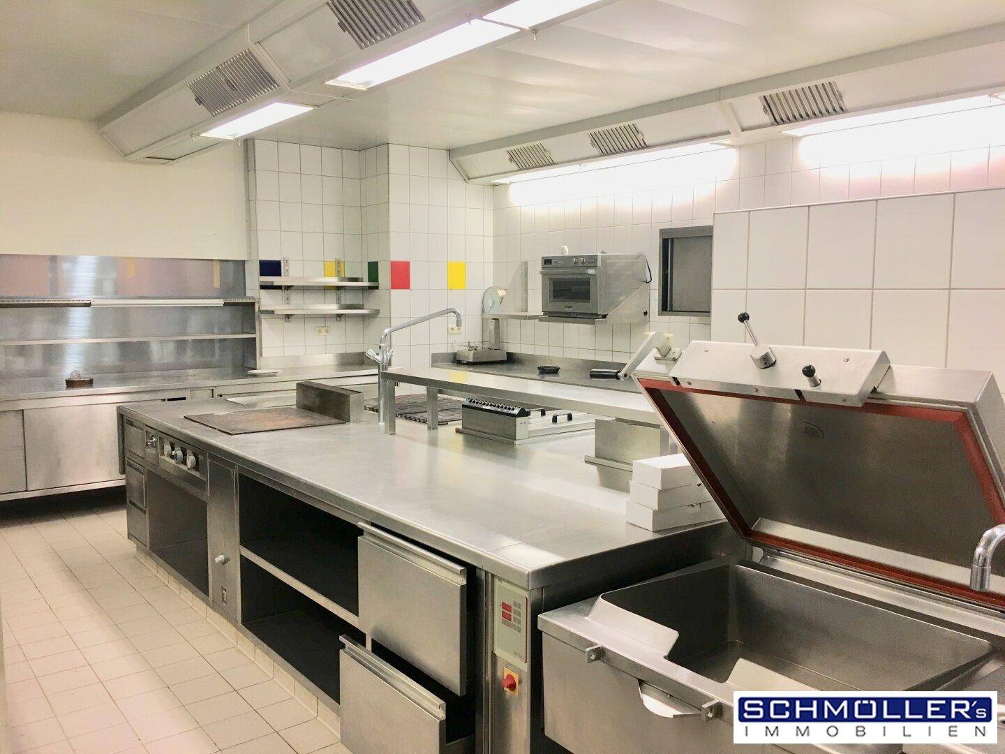 Professionelle Großküche mit Edelstahlgeräten, Fliesenwänden und industrieller Beleuchtung.