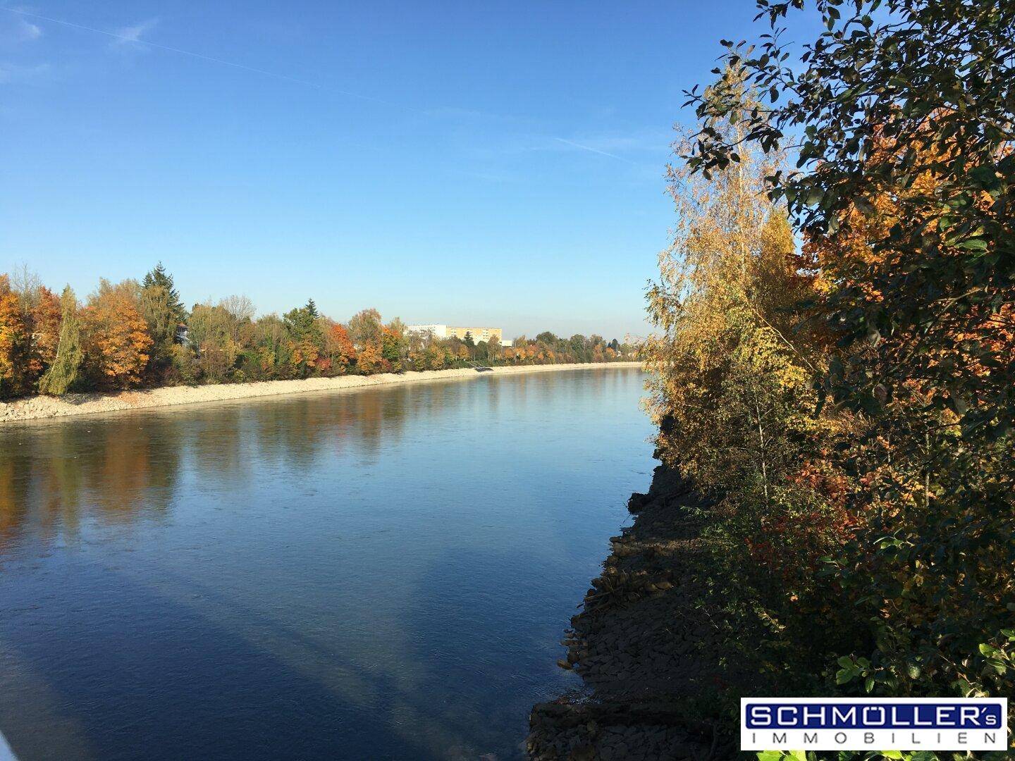 Malerischer Flusslauf mit herbstlich gefärbten Bäumen am Ufer unter einem strahlend blauen Himmel.