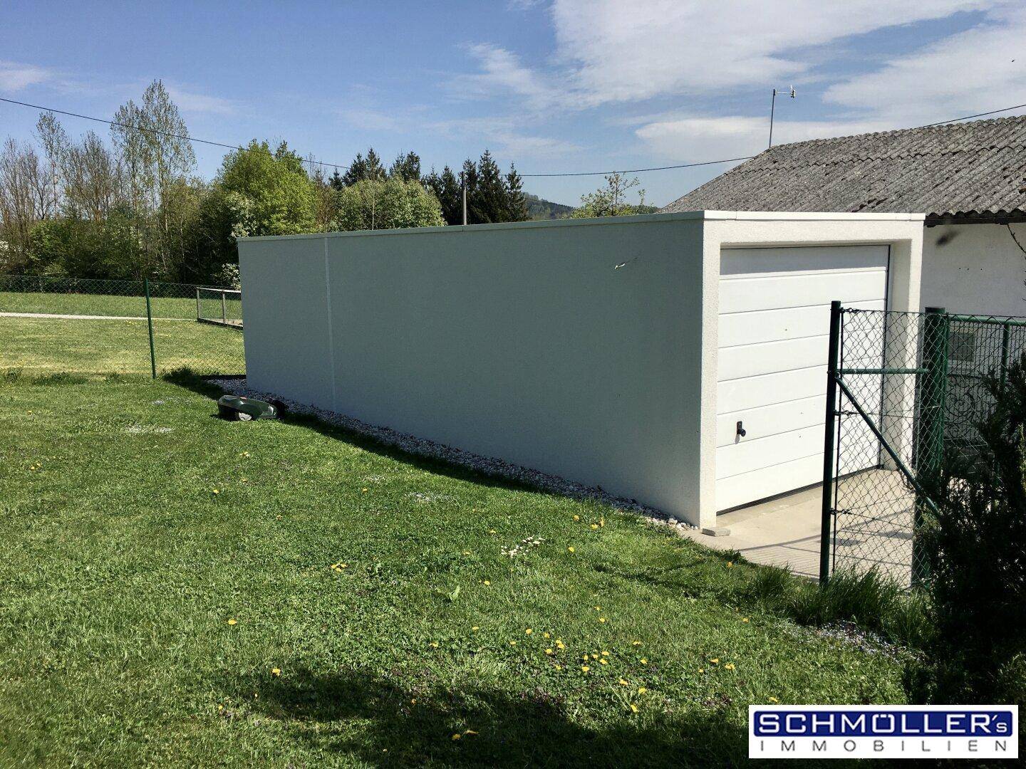Freistehende Garage mit weißem Tor und umliegender Rasenfläche.