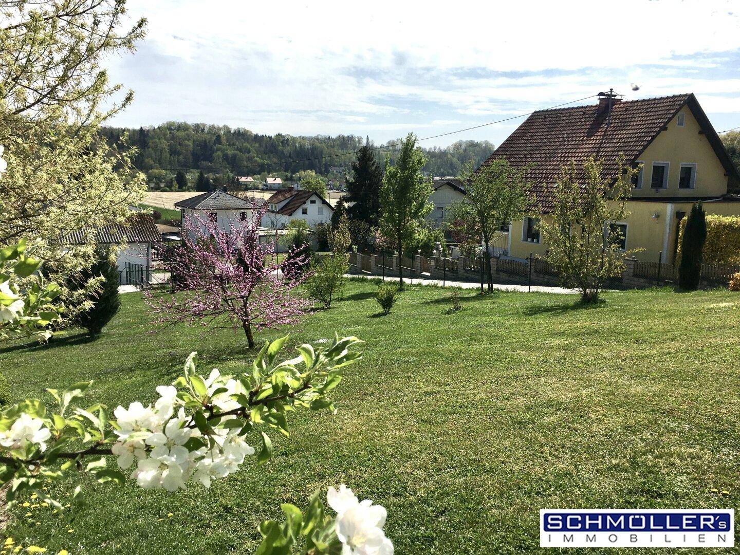 Sonniger Garten mit blühenden Sträuchern und weitem Blick über die Landschaft.