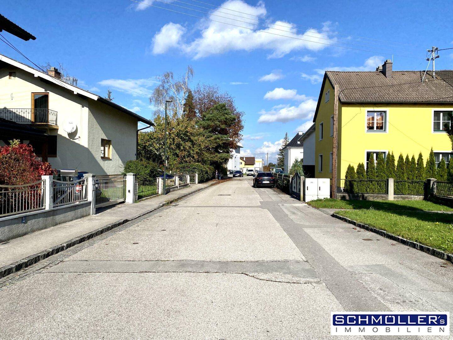 Ruhige Wohnstraße mit gepflegten Häusern und Bäumen unter einem sonnigen Herbsthimmel.