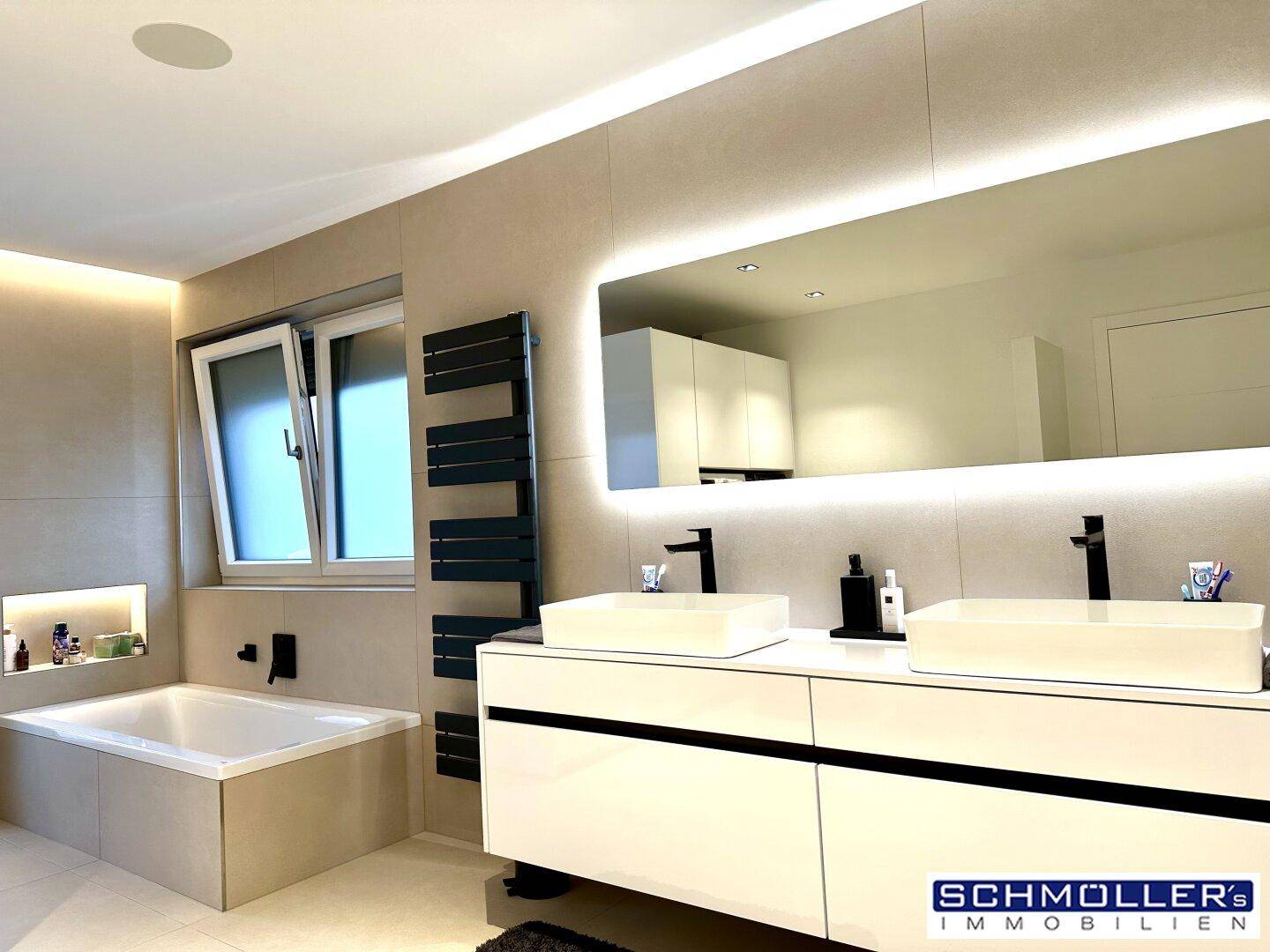 Modernes Badezimmer mit Doppelwaschbecken, Badewanne und beleuchtetem Spiegel.
