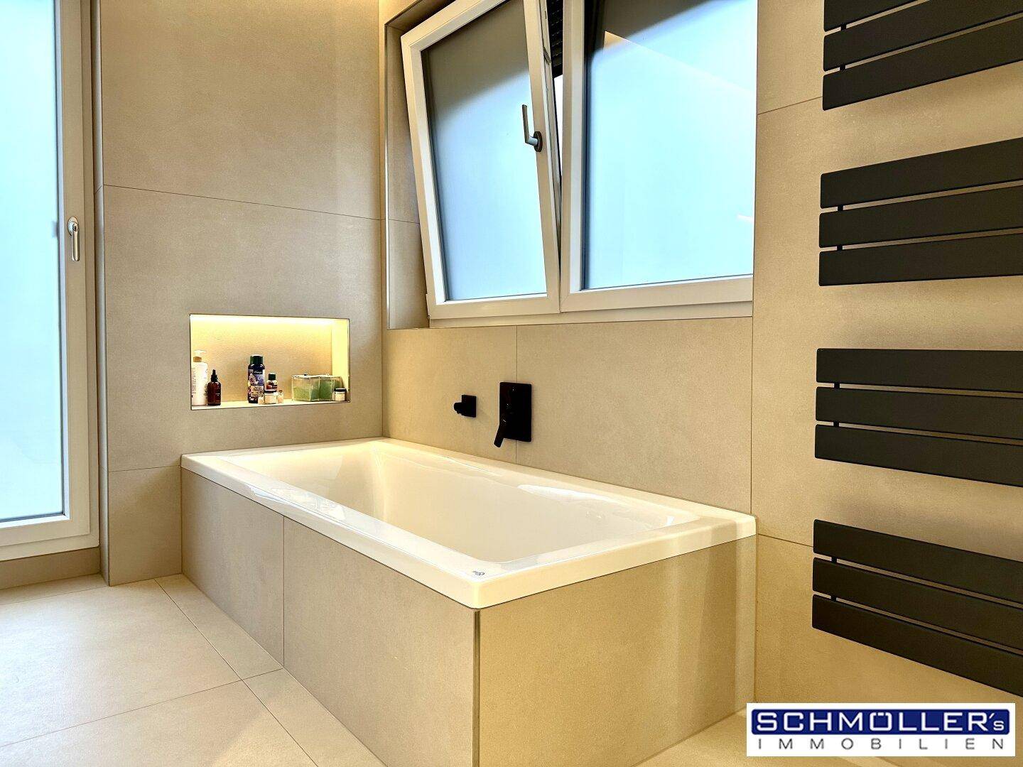 Eingebaute Badewanne in einem modernen Badezimmer mit Fliesen und Fenster.
