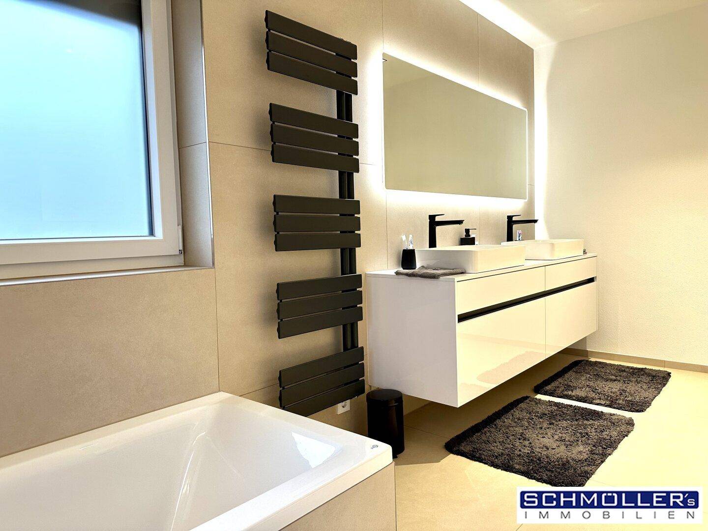 Elegantes Badezimmer mit Badewanne, beheiztem Handtuchhalter und großem Spiegel.