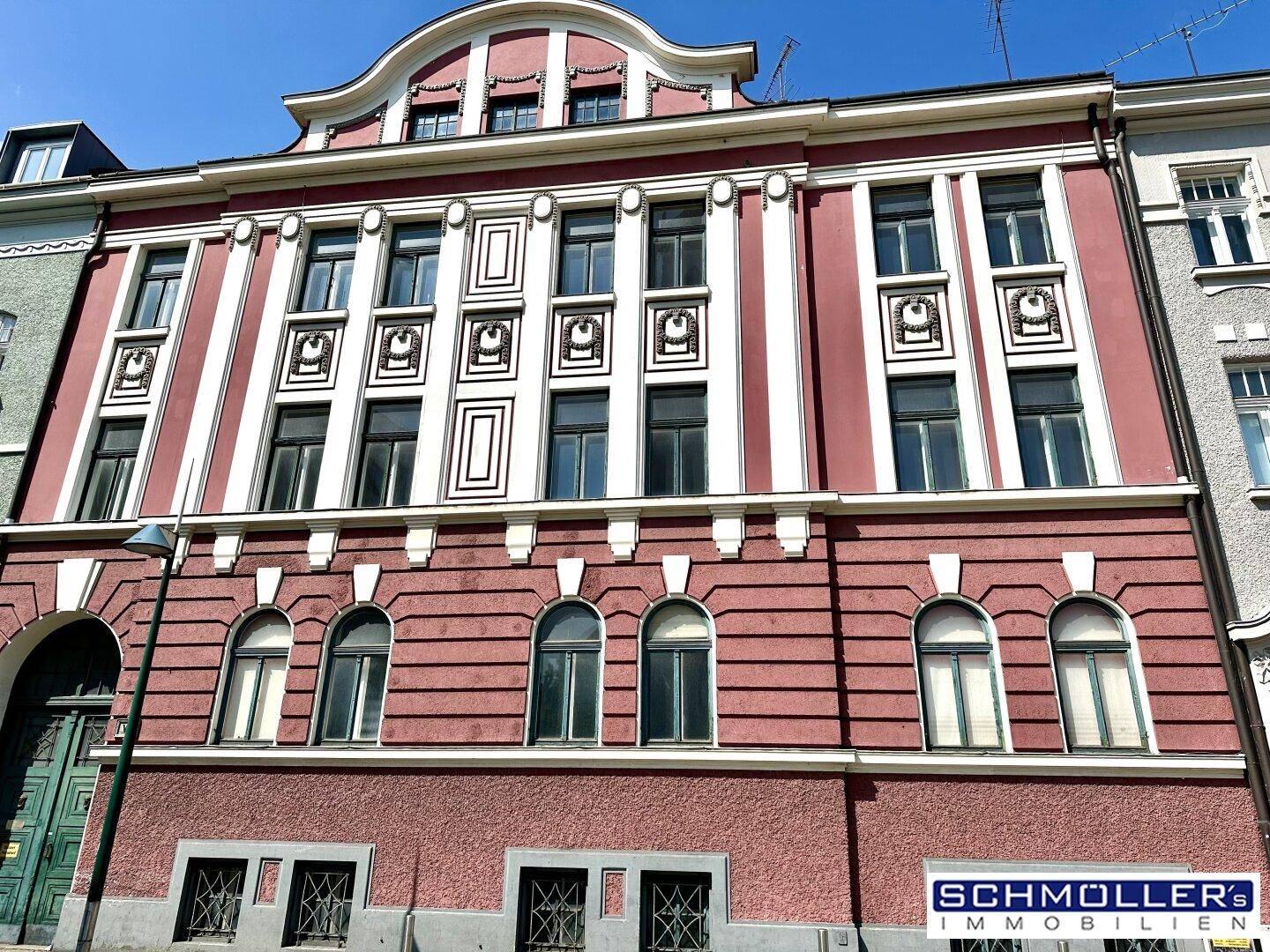Historisches Gebäude mit rosa Fassade, dekorativen Elementen und vielen Fenstern.
