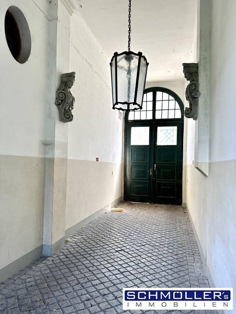 Historischer Eingangsbereich mit gefliestem Boden, Bogenfenster und dekorativer Deckenleuchte.