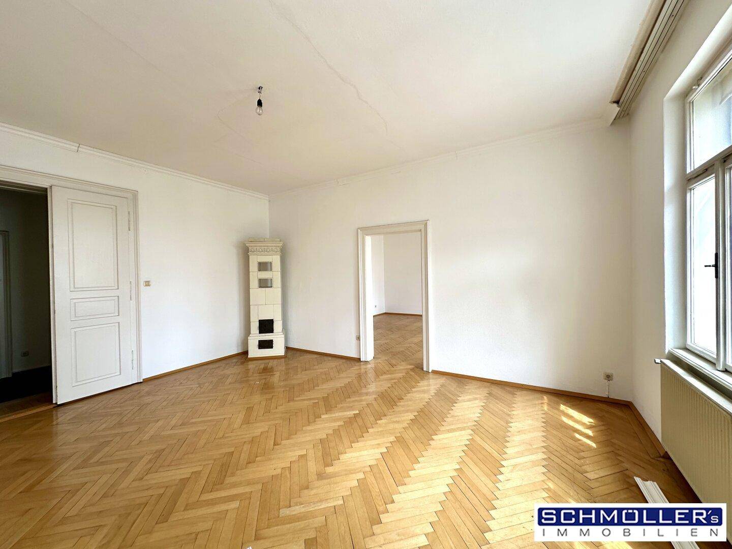 Großes Wohnzimmer mit Fischgrätparkett, Kachelofen und hohen Decken in einem Altbau.