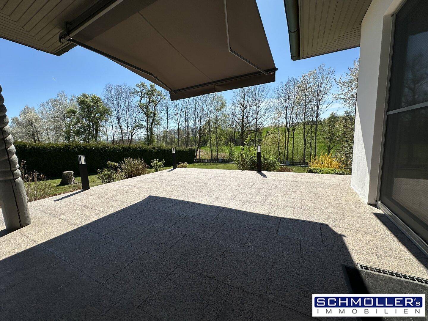 Weitläufige Terrasse mit Granitplatten und Blick auf den gepflegten Garten und die umliegende Natur.