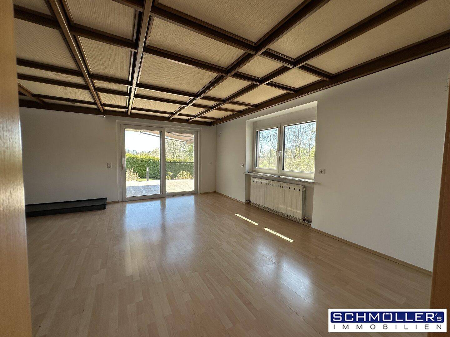 Helles Wohnzimmer mit Parkettboden, Holzbalkendecke und großen Fenstern mit Blick ins Grüne.
