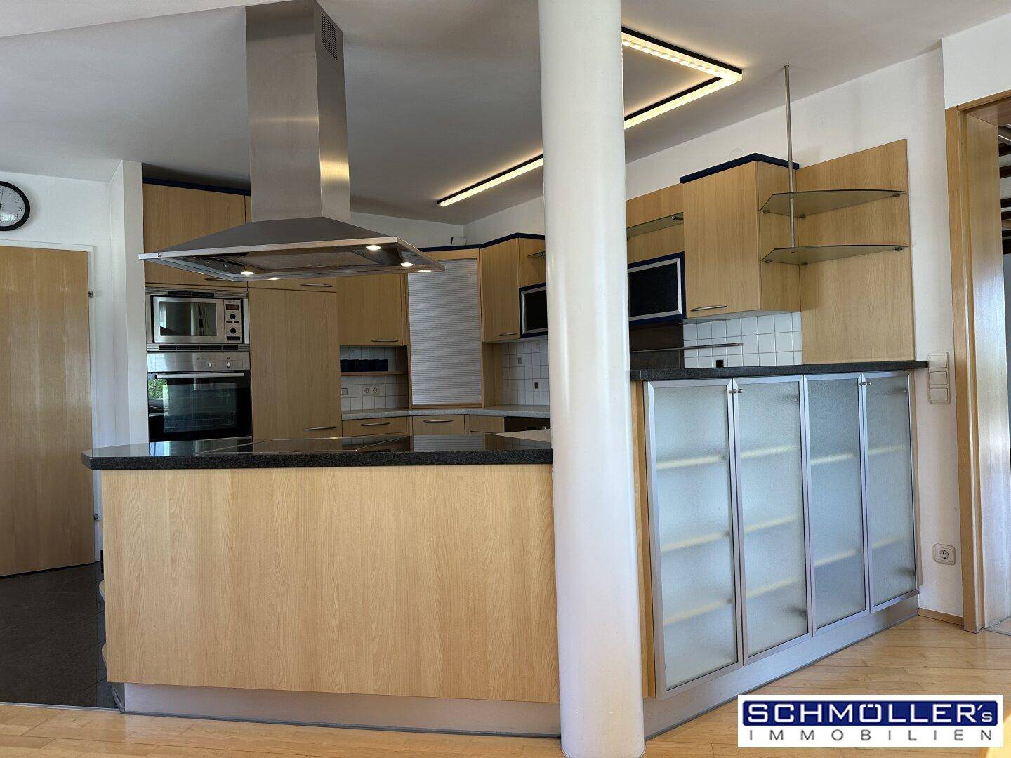 Moderne Einbauküche mit Holzfronten, Kochinsel und integrierten Edelstahlgeräten in einem offenen Wohnbereich.