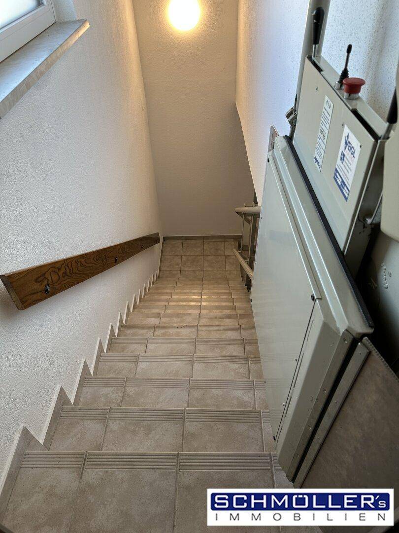 Geflieste Treppe mit installiertem Treppenlift und Holzhandlauf für Barrierefreiheit.