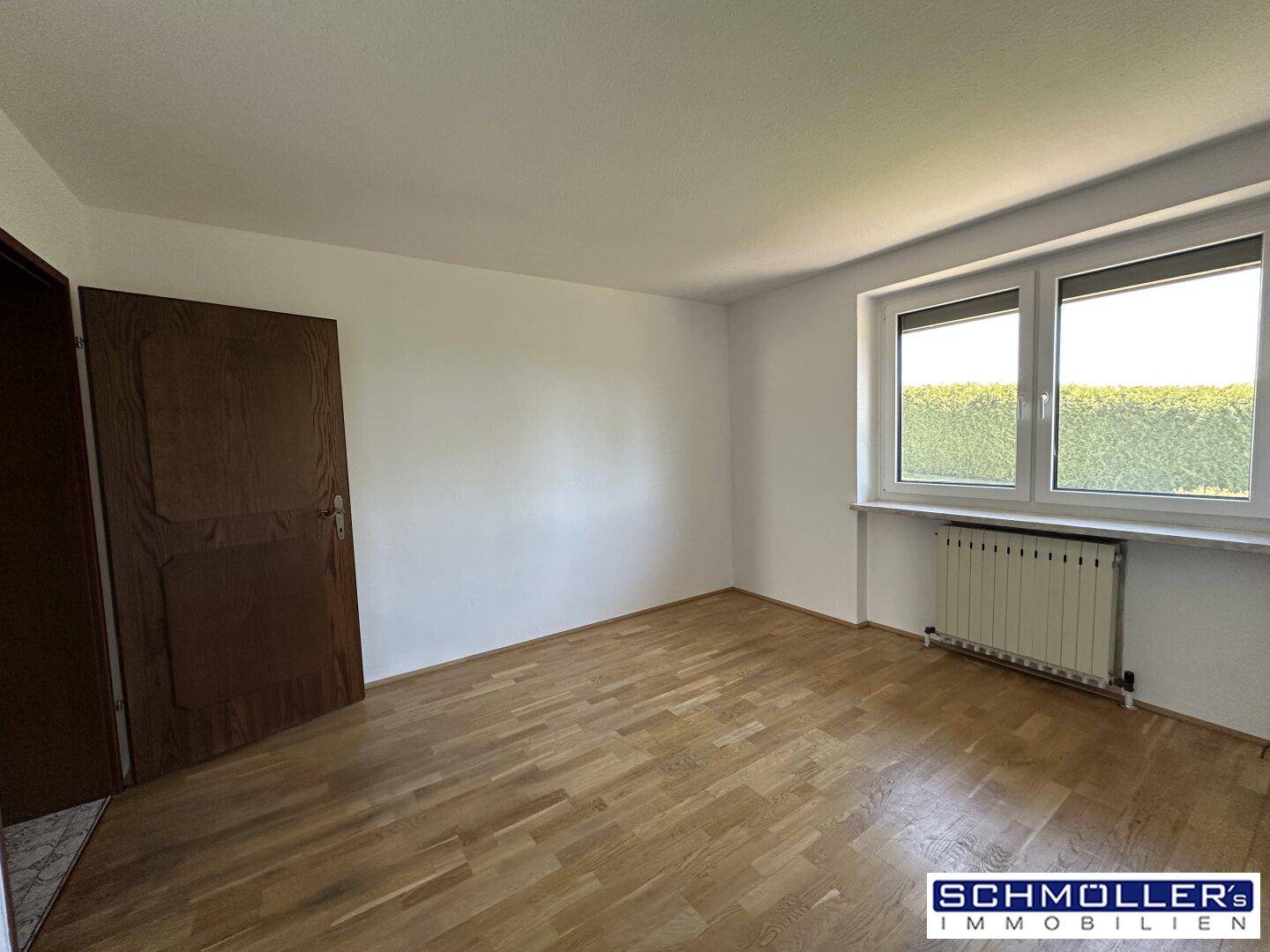 Freundliches Zimmer mit hellem Parkettboden, weiß gestrichenen Wänden und einer Holztür.