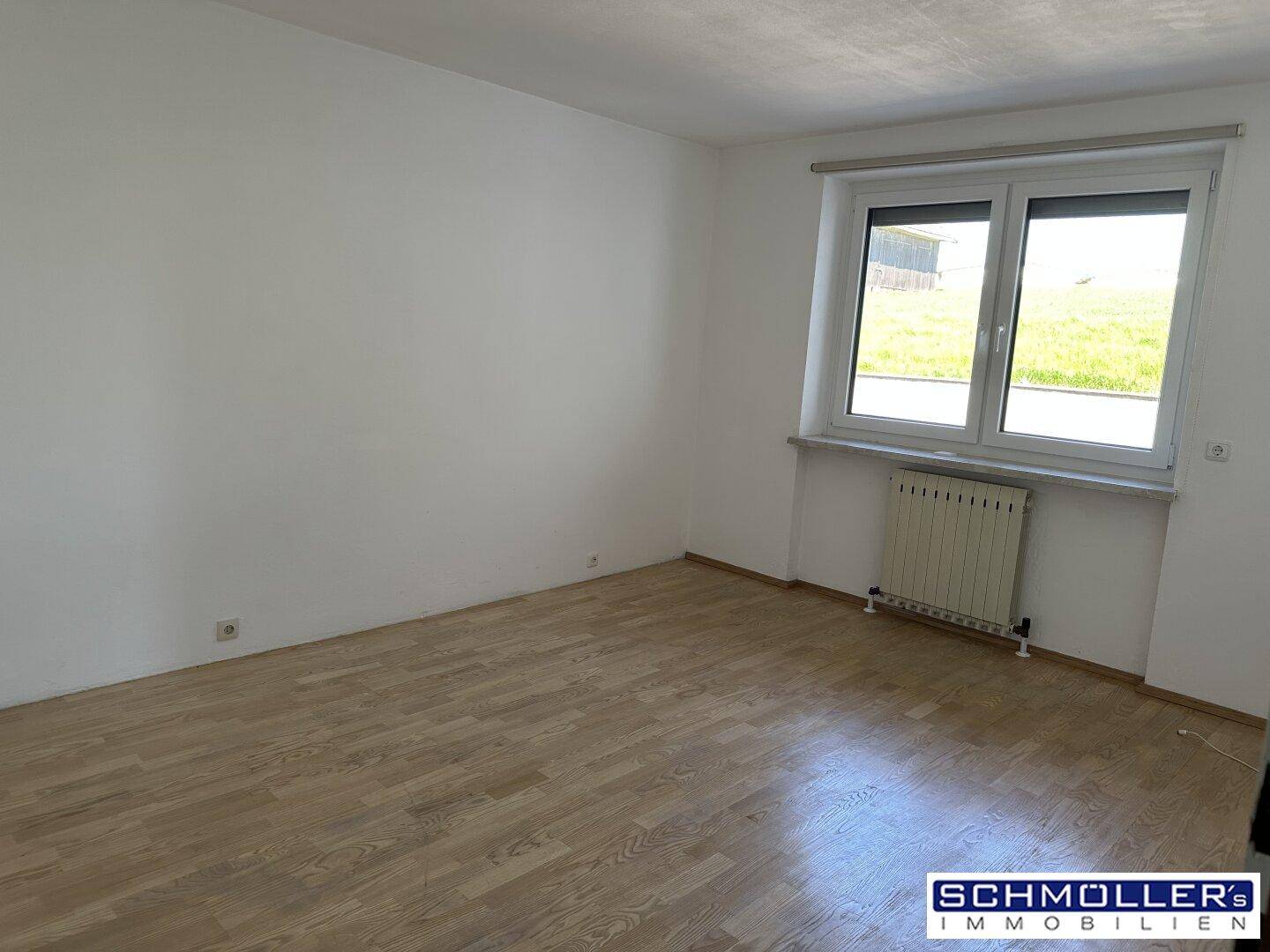 Schlafzimmer mit Parkettboden, weiß gestrichenen Wänden und Blick ins Grüne durch das Fenster.