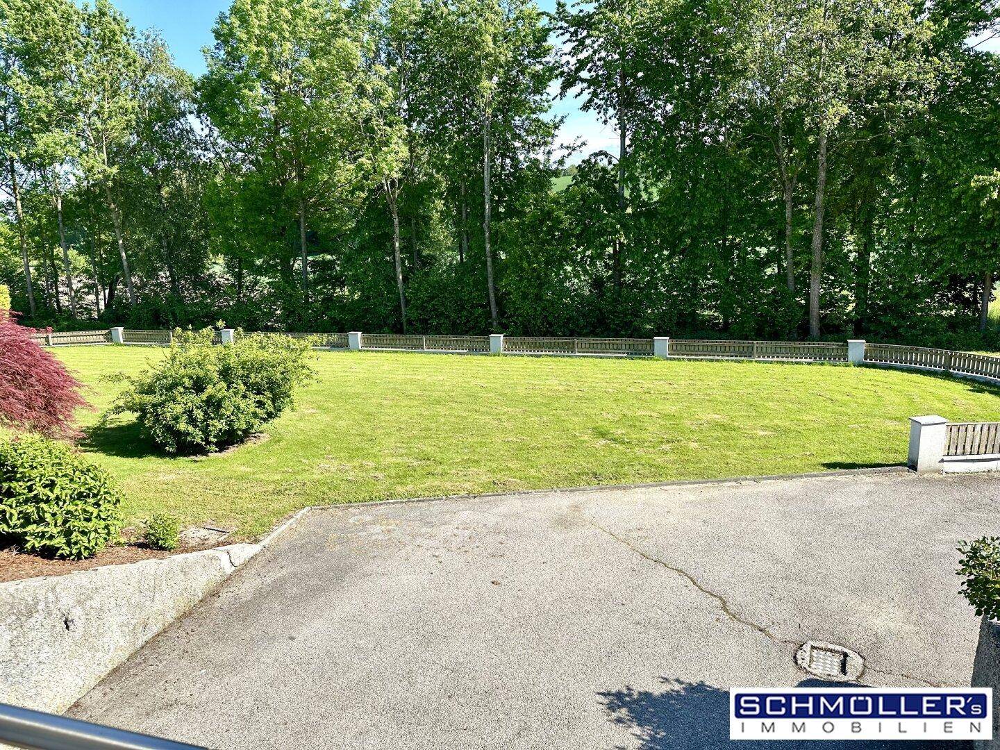 Gepflegter Garten mit weitläufiger Rasenfläche und dekorativen Zaunelementen im Hintergrund, von oben betrachtet.