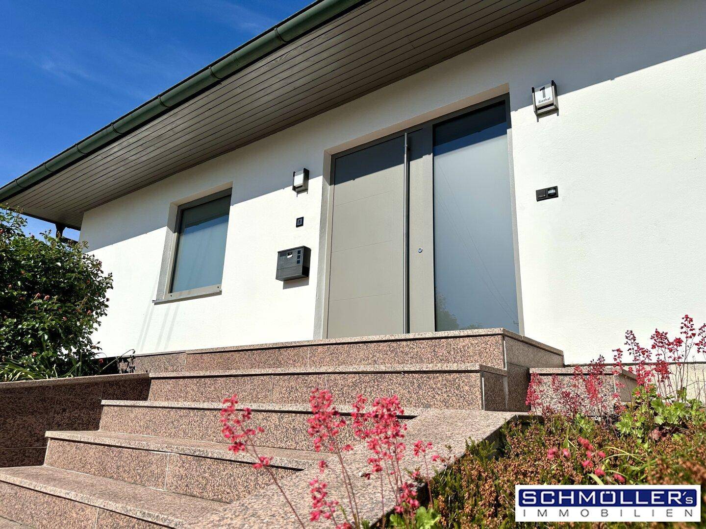 Moderner Hauseingang mit breiter Granittreppe und einer eleganten Haustür unter klarem Himmel.
