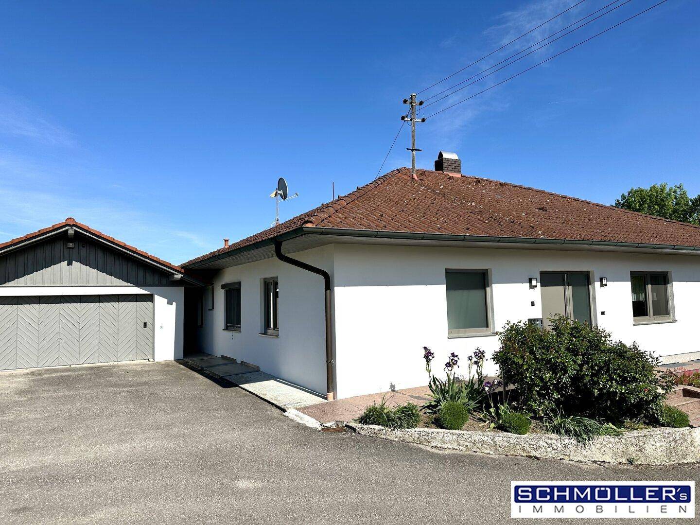 Seitenansicht des Hauses mit separater Garage und gepflegtem Vorgartenbereich unter blauem Himmel.