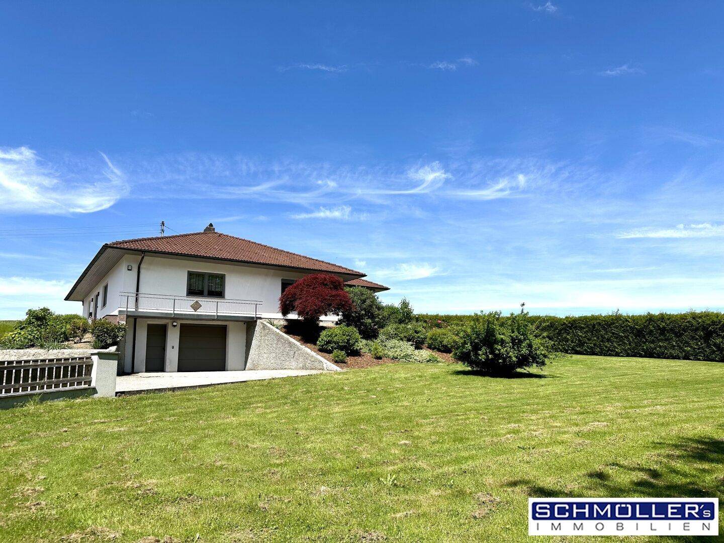 Freistehendes Einfamilienhaus mit großem Garten und integrierter Garage im Untergeschoss, umgeben von Natur.