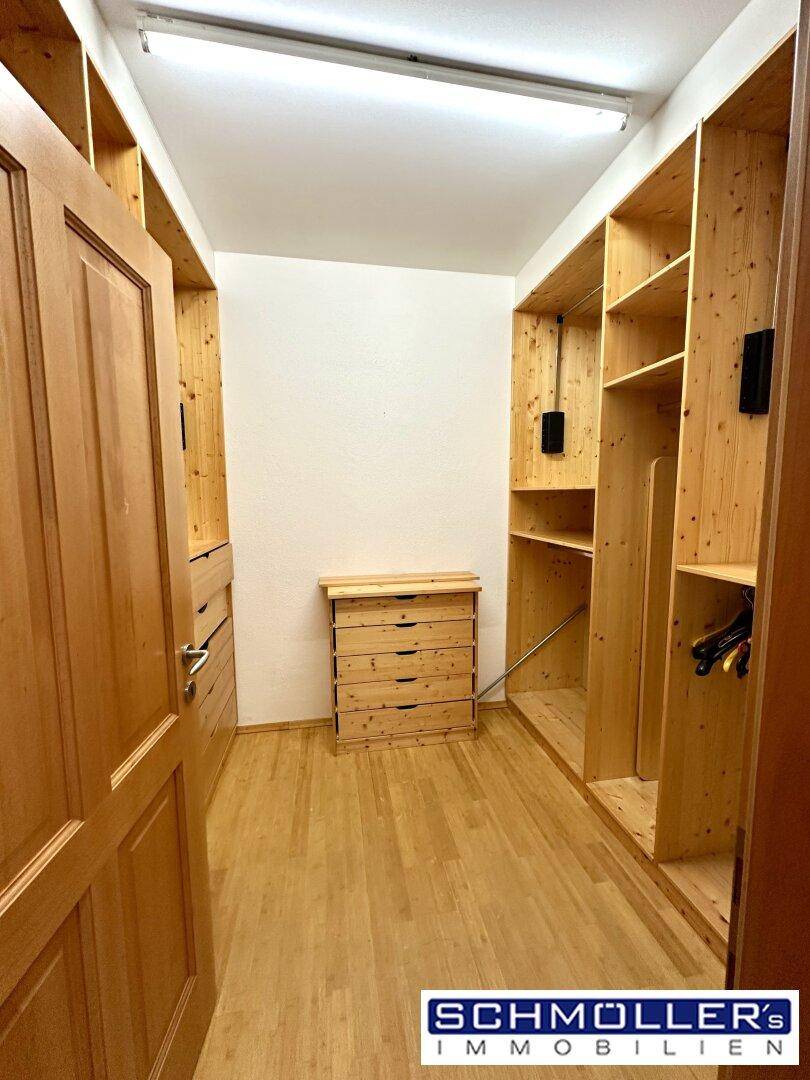Heller begehbarer Kleiderschrank mit umfangreichem Holzregalsystem und integrierter Kommode.