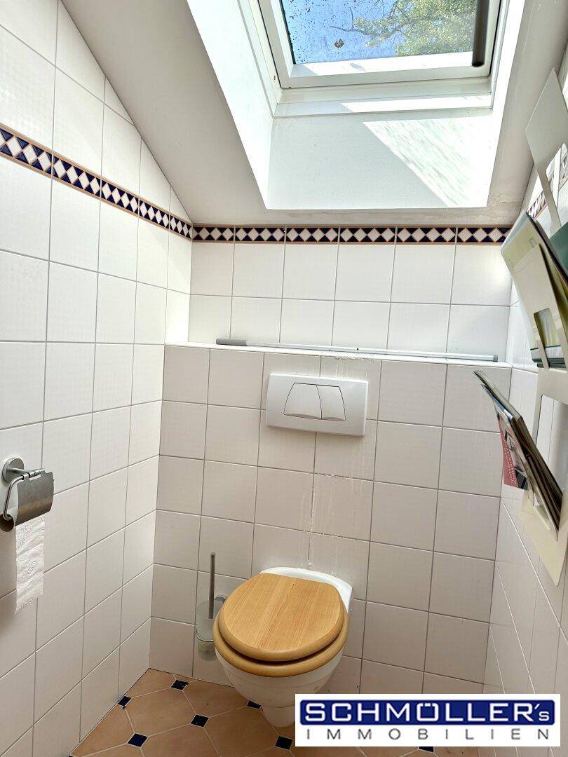 Kleines WC mit weißen Fliesen, Dachfenster und farbiger Bordüre, hell und funktional.