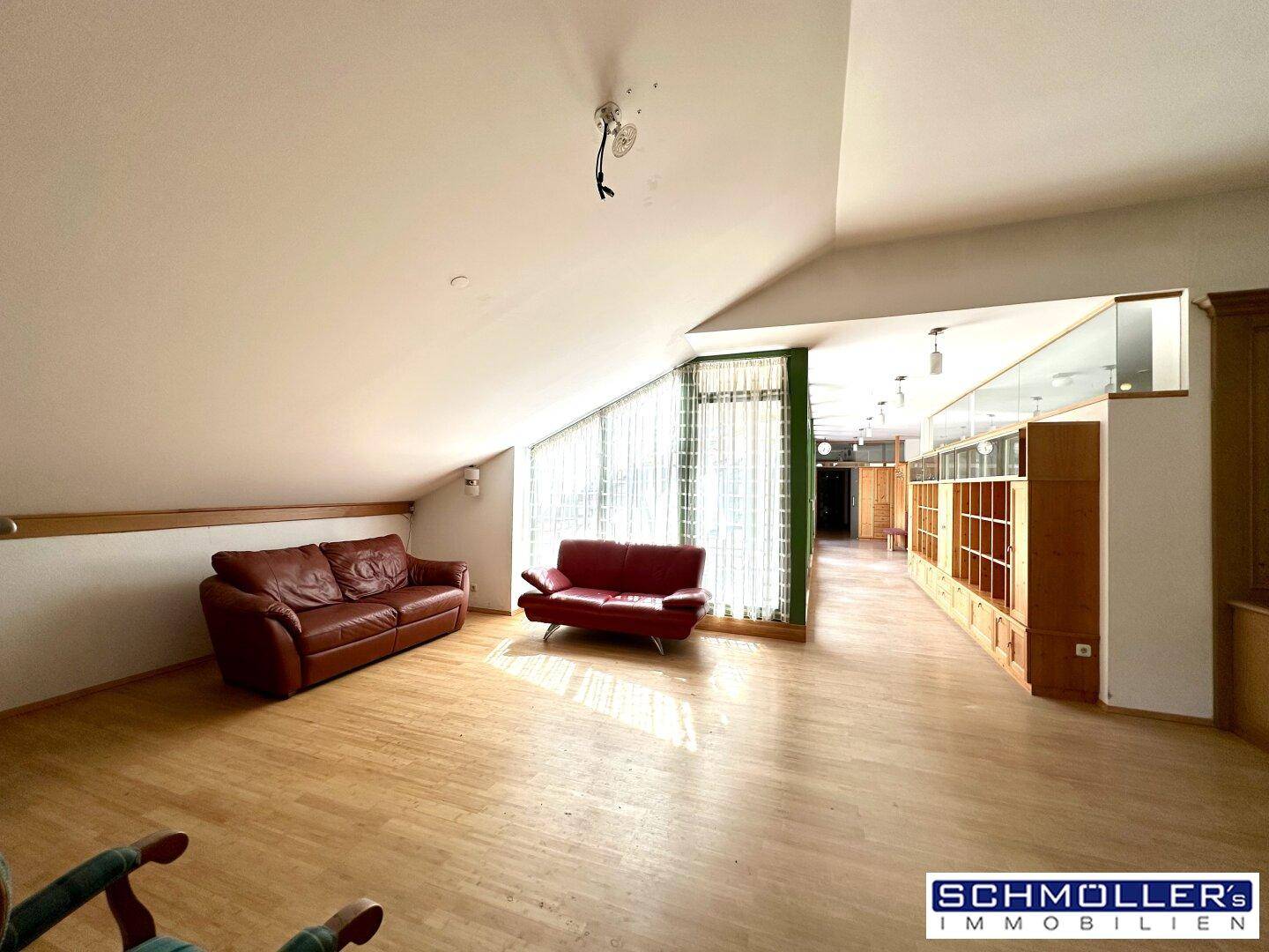 Helles Wohnzimmer mit zwei Ledersofas, Holzboden und einer charakteristischen Dachschräge.