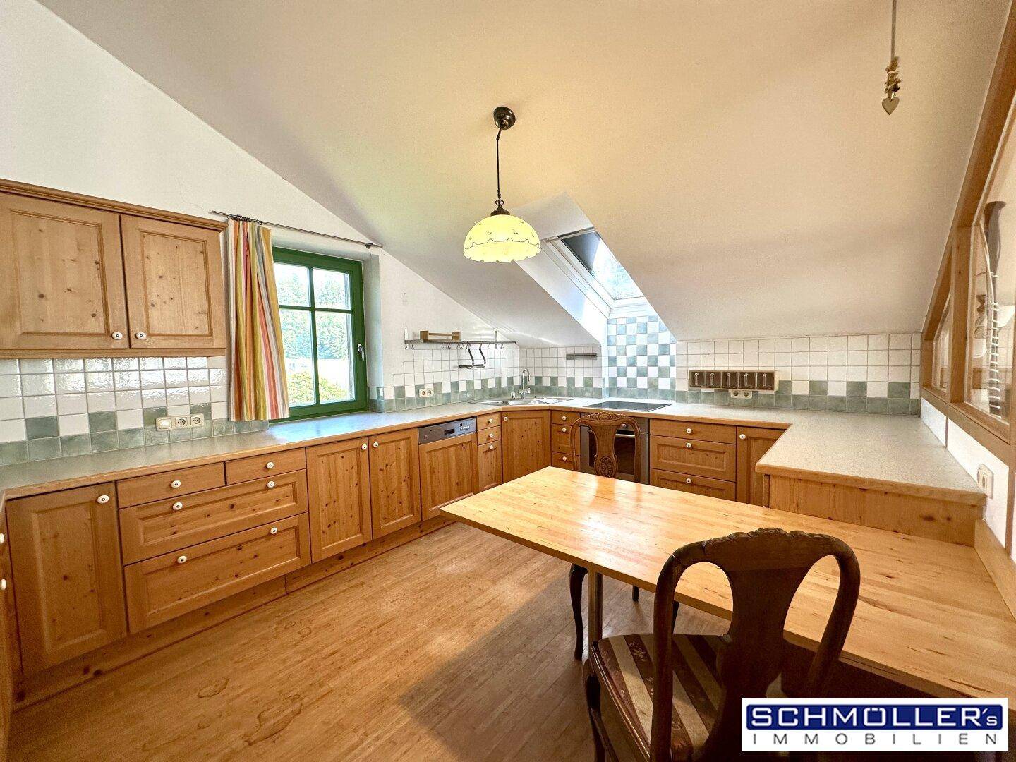 Traditionelle Küche im Dachgeschoss mit Holzschränken, Dachfenster und Essbereich.