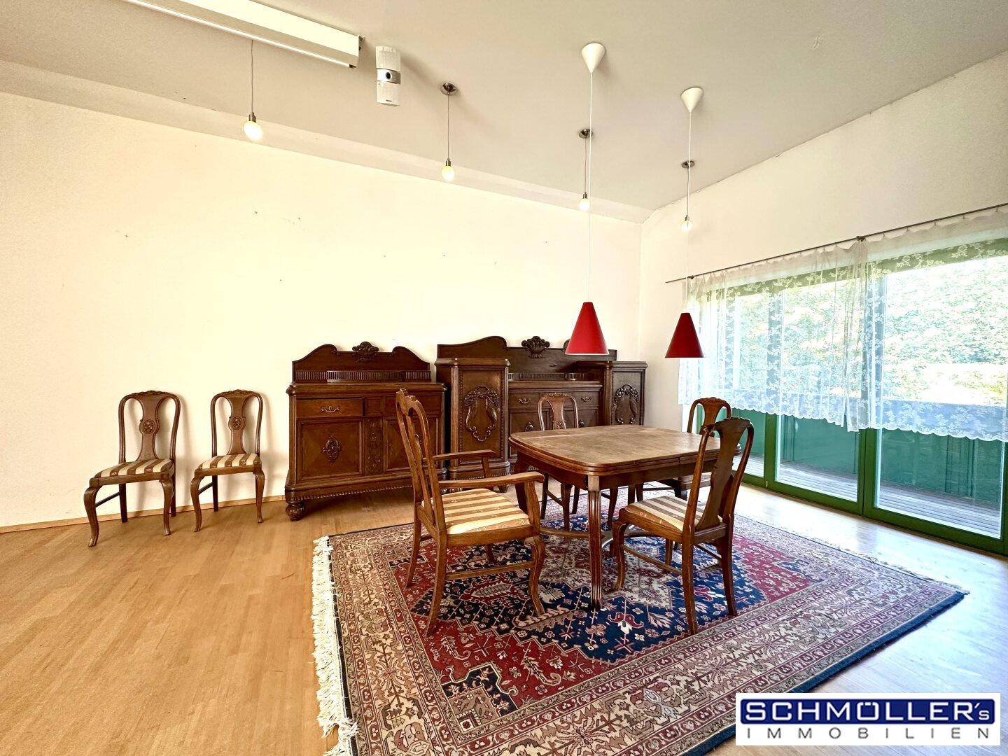 Geräumiger Wohn-Essbereich mit antiken Holzmöbeln, Teppich und Zugang zu einem Balkon.