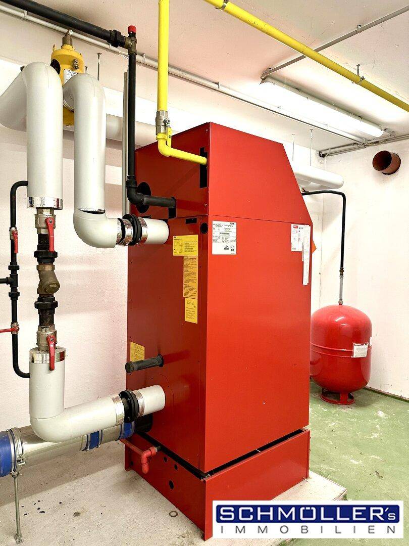 Technikraum mit großem roten Heizkessel und sichtbaren Rohrleitungen für die Gebäudetechnik.