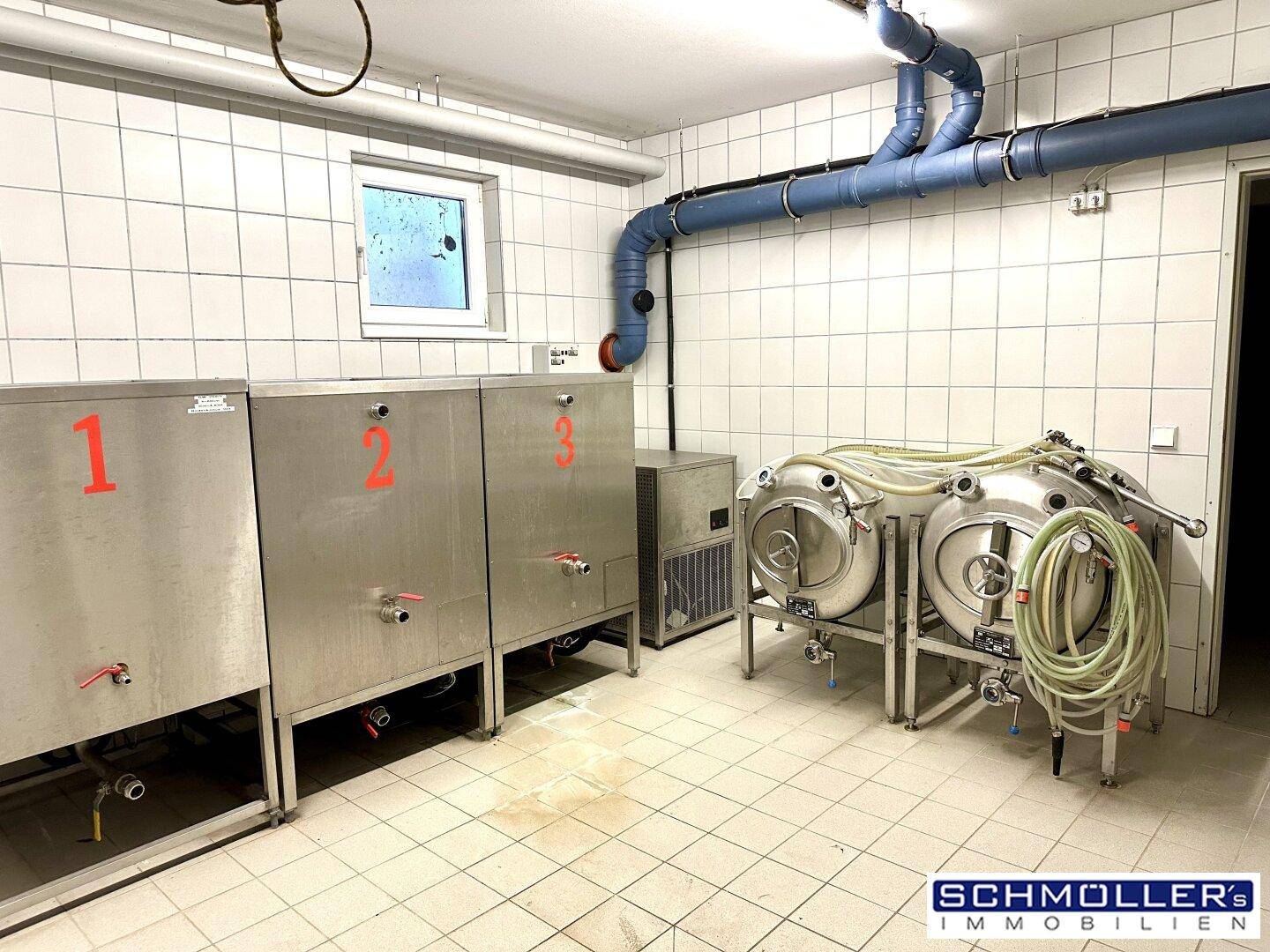 Gefliester Kellerraum mit industriellen Tanks und Rohren, ideal für Lagerung oder Produktion.