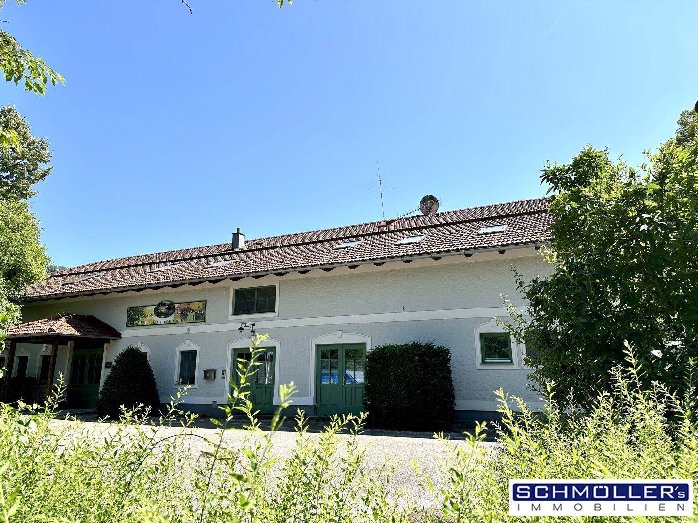 Weitläufige Ansicht des Landhauses mit seiner Fassade und dem umliegenden Grün unter klarem Himmel.
