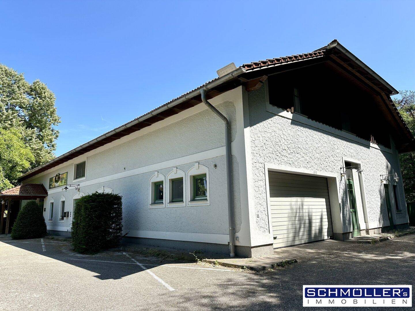 Seitenansicht des Landhauses mit einer großen Garagentür und einem gepflasterten Parkplatzbereich.