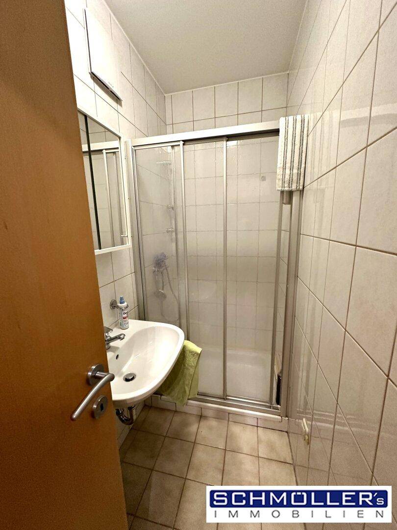 Gefliestes Badezimmer mit Duschkabine, Waschbecken und einem Spiegel, in gutem Zustand.