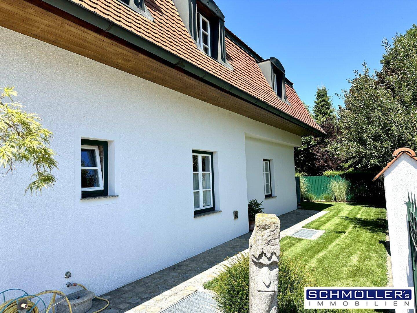 Seitenansicht des Hauses mit gepflegtem Rasen, kleinen Fenstern und einem sonnigen Gartenbereich.