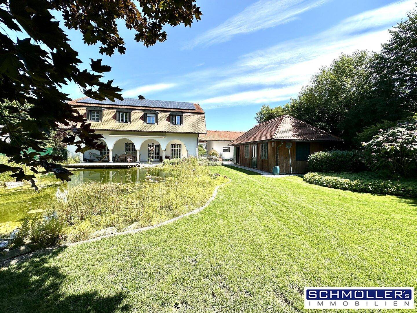 Weitläufiger Garten mit Teich und Blick auf das Haus mit Solaranlage auf dem Dach.