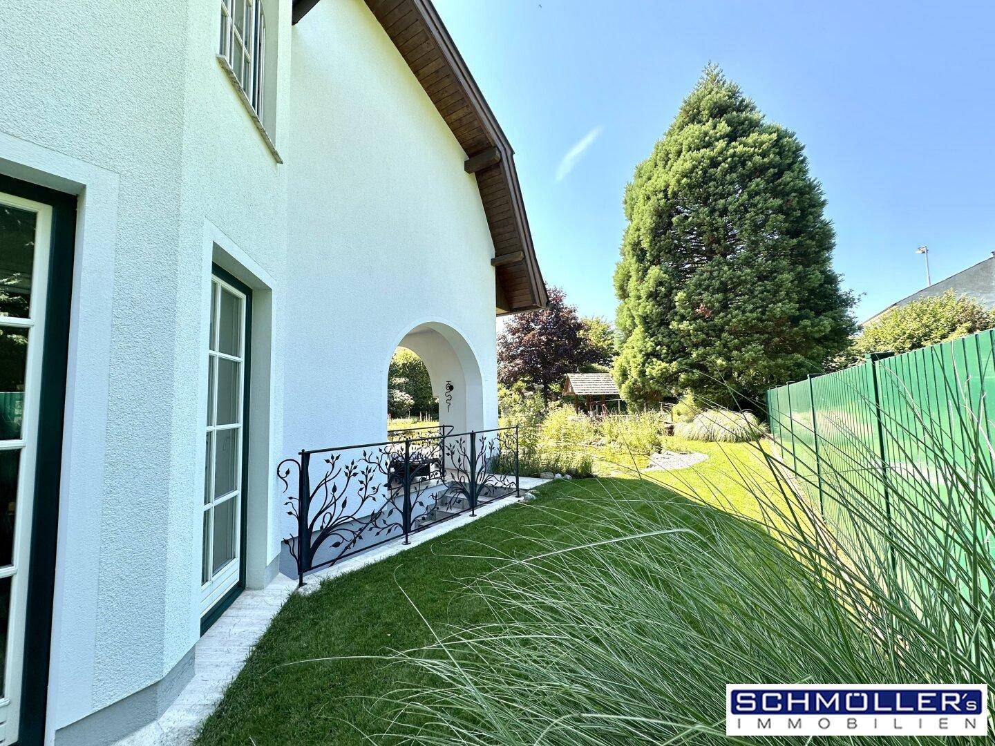 Seitenansicht des Hauses mit einer kleinen Terrasse und dekorativem Geländer zum Garten hin.