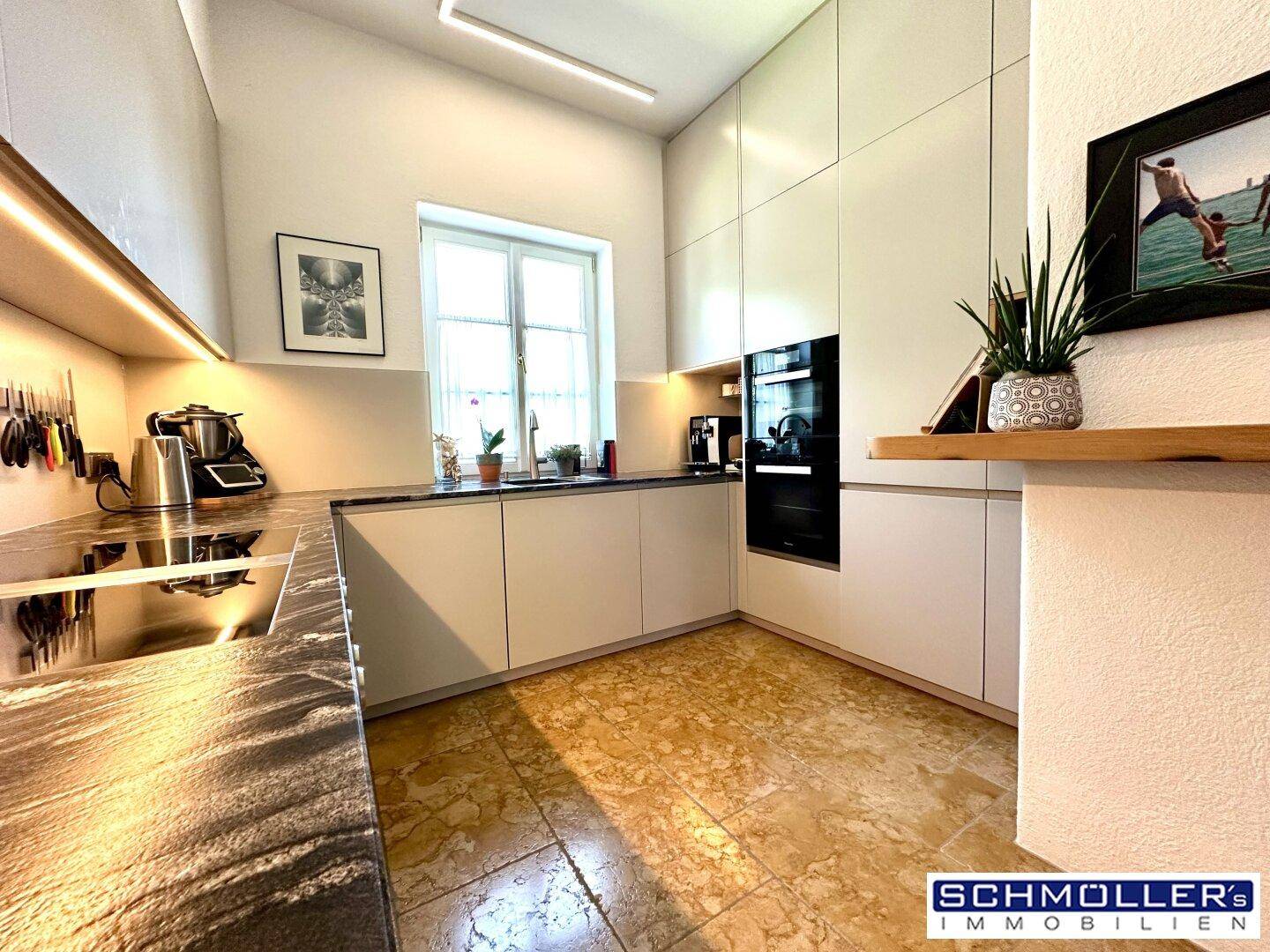 Moderne Küche mit weißen Schränken, dunkler Arbeitsplatte und Fenster für Tageslicht.