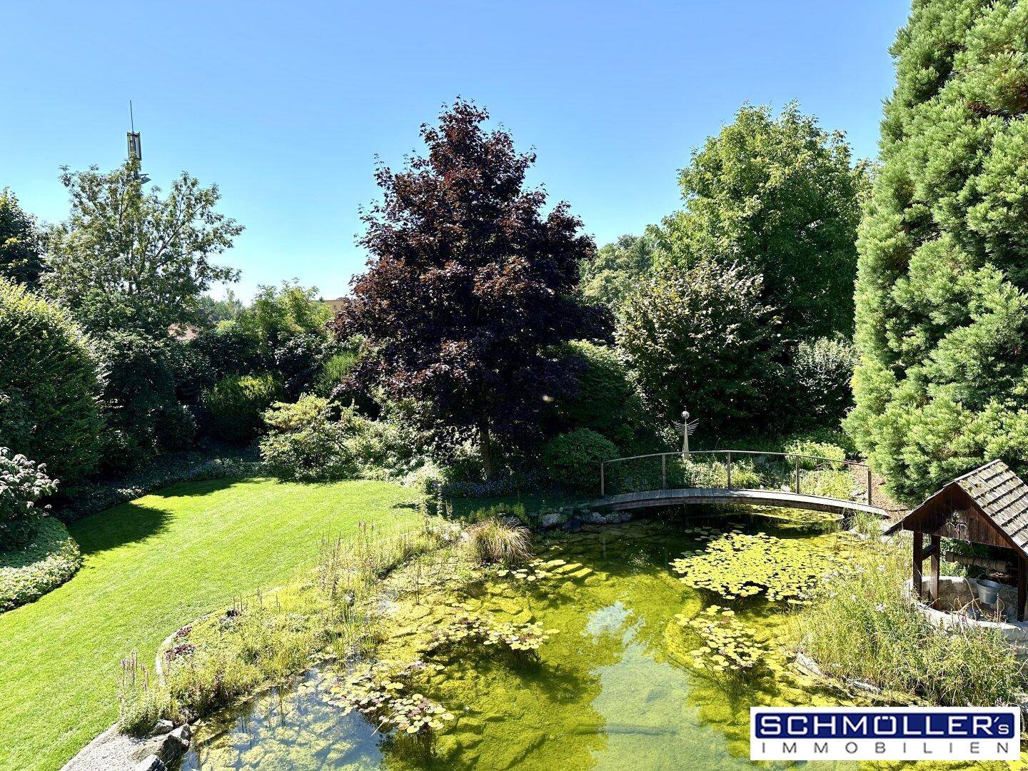 Malerischer Garten mit Teich, kleiner Brücke und üppiger grüner Vegetation.