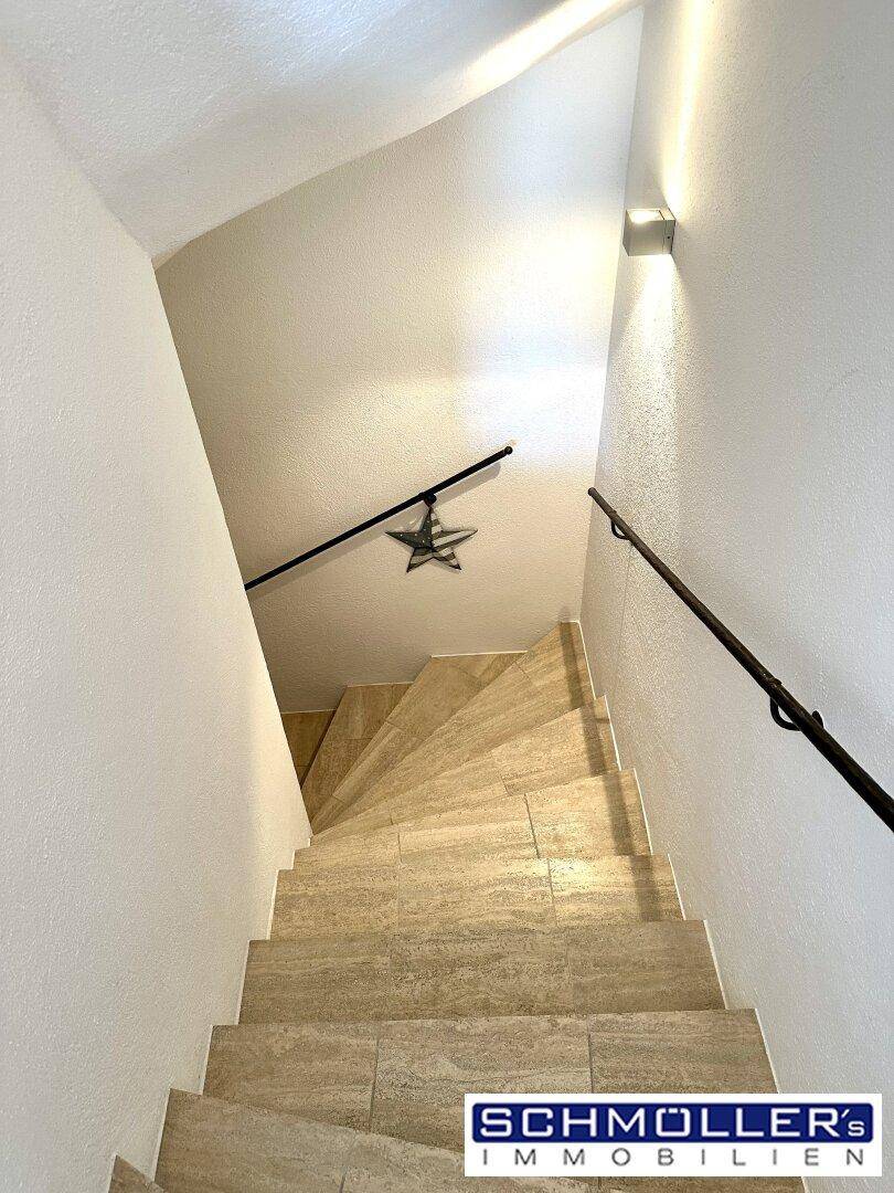 Moderne Treppe mit Fliesenstufen und schlichtem Geländer, gut beleuchtet.