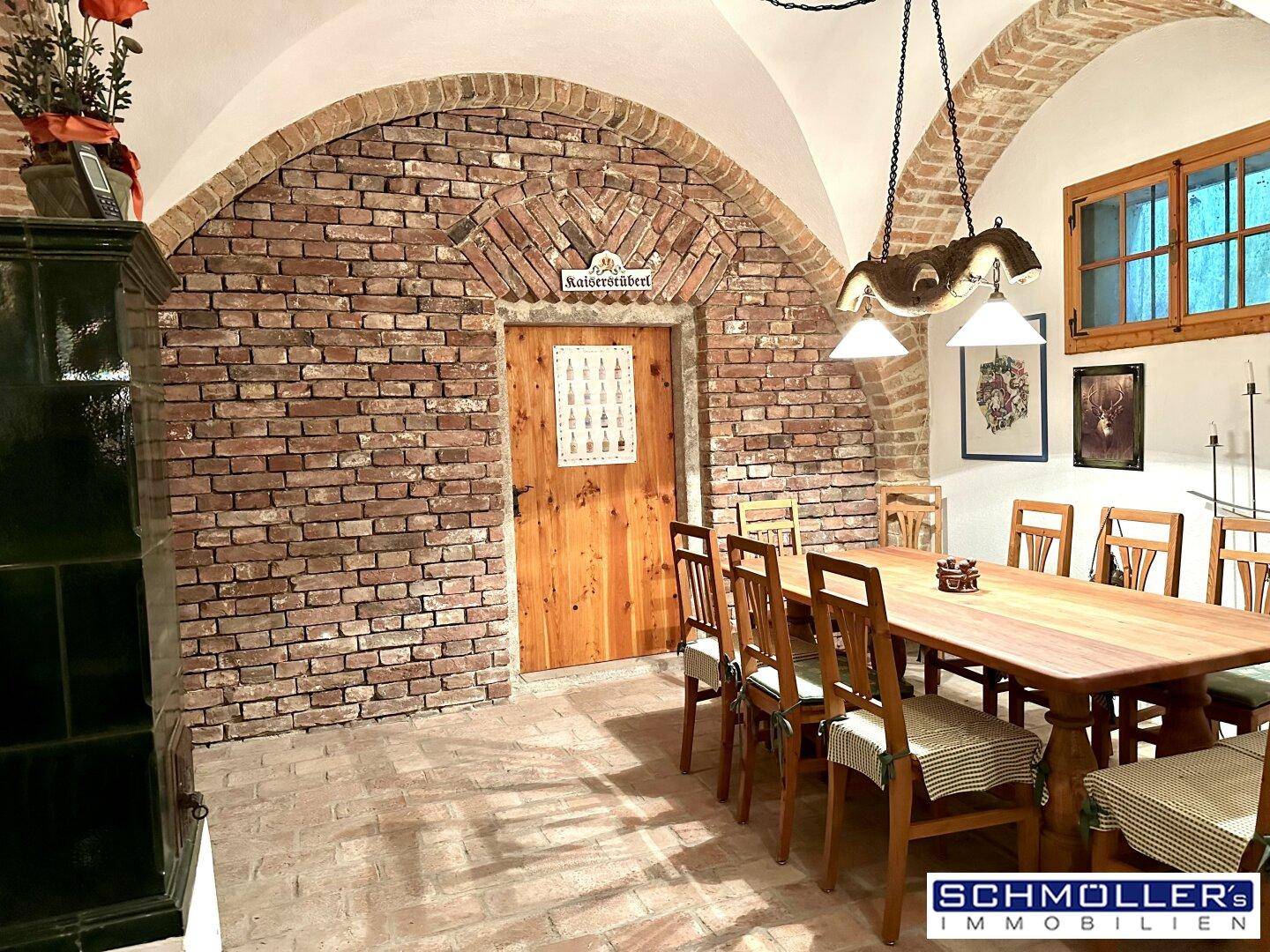 Gemütlicher Essbereich mit Ziegelwänden, Holztisch und traditionellem Kachelofen.