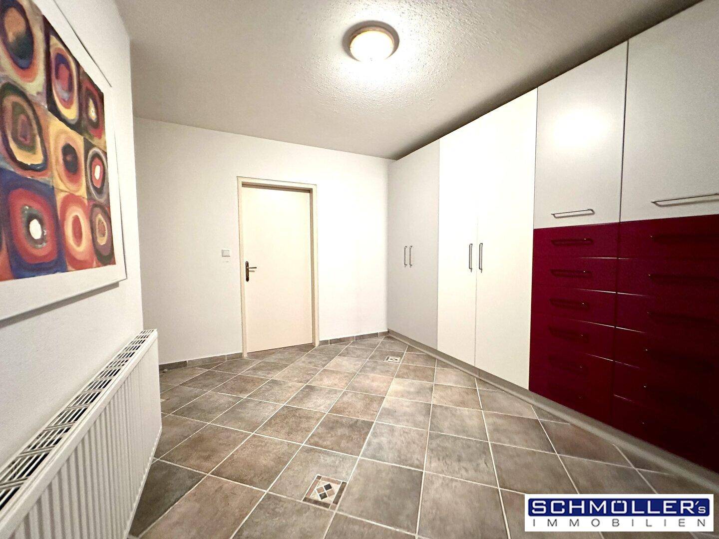 Raum mit Fliesenboden und modernen Einbauschränken in Weiß und Rot.