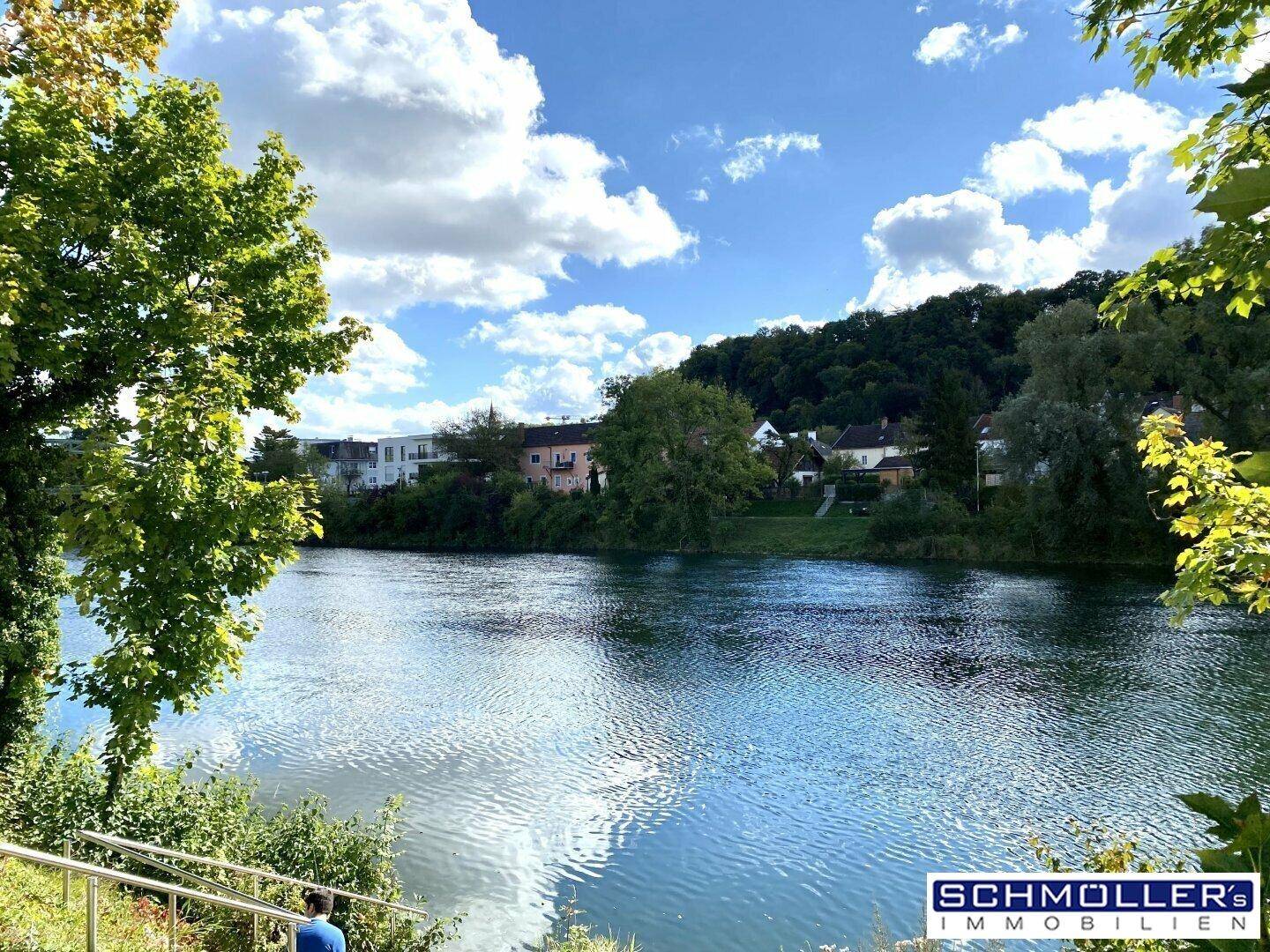 Weitläufiger Blick auf einen Fluss oder See mit bewaldeten Ufern und Häusern in der Ferne.