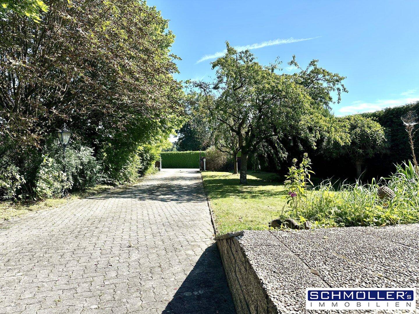 Lange gepflasterte Auffahrt, umgeben von üppigem Grün und Bäumen, die zum Grundstück führt.