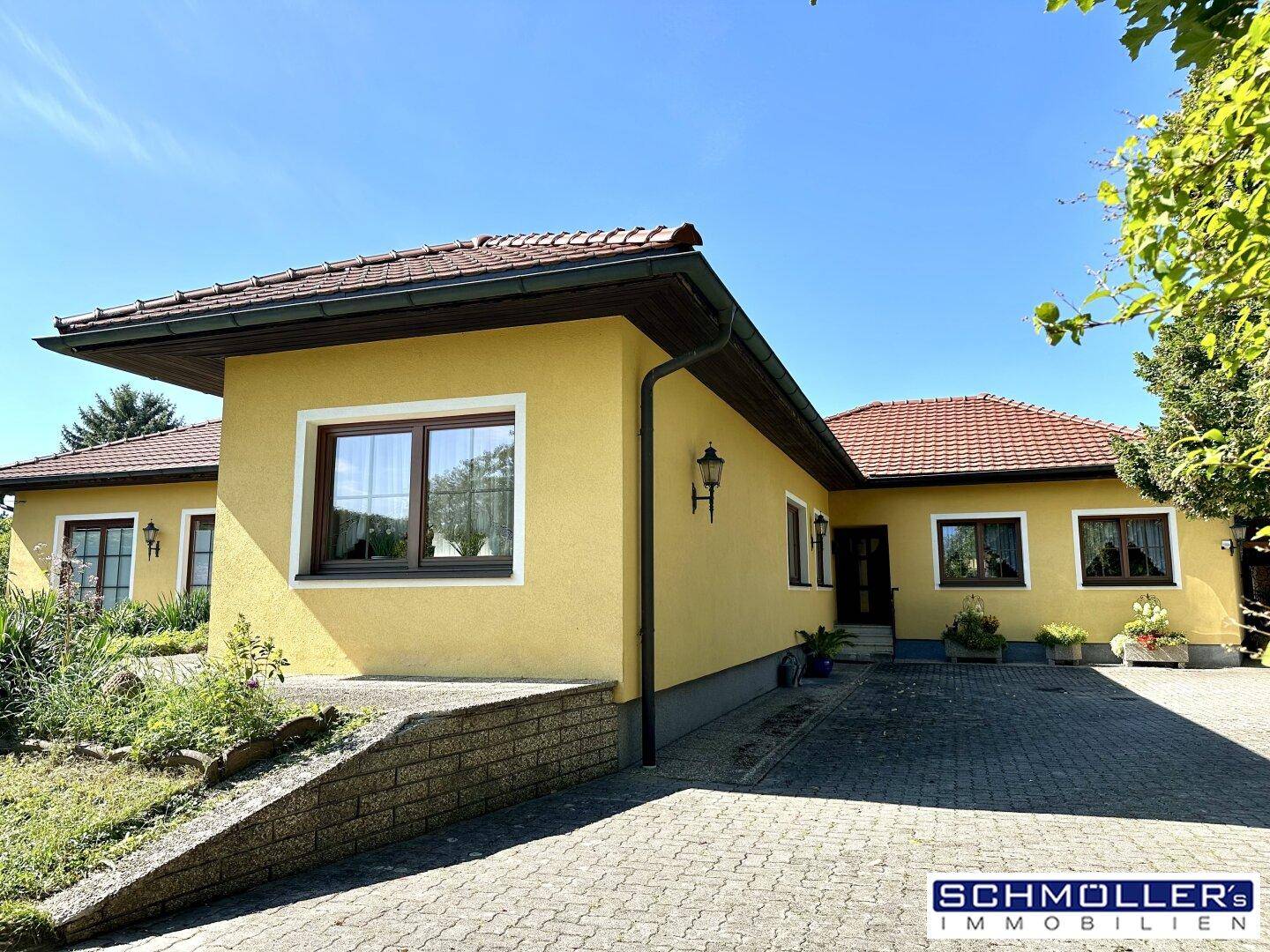 Gelbes Haus mit rotem Ziegeldach und gepflasterter Auffahrt, umgeben von gepflegter Grünfläche.
