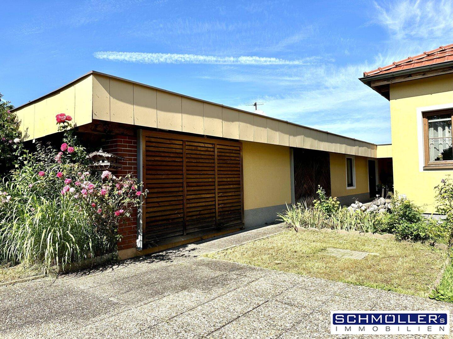 Geräumige Garage mit Holzlamellentor, umgeben von Blumen und Grünflächen neben dem Haus.